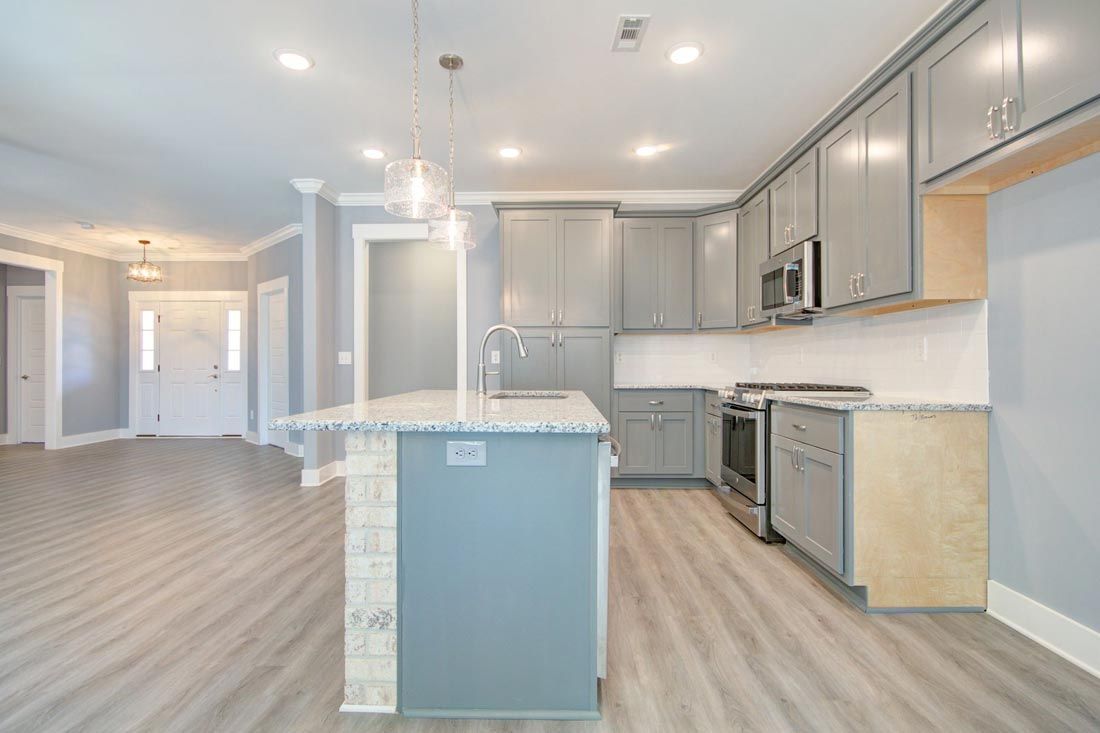 A modern kitchen with grey cabinets, light wood-look flooring, a kitchen island, and stainless steel appliances.