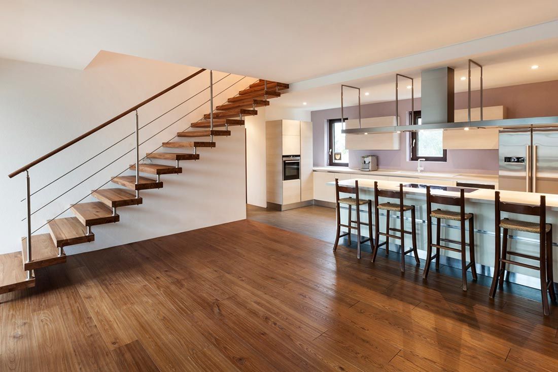 A modern, open-concept room featuring a wooden floating staircase, hardwood floors, and a kitchen island with bar stools.