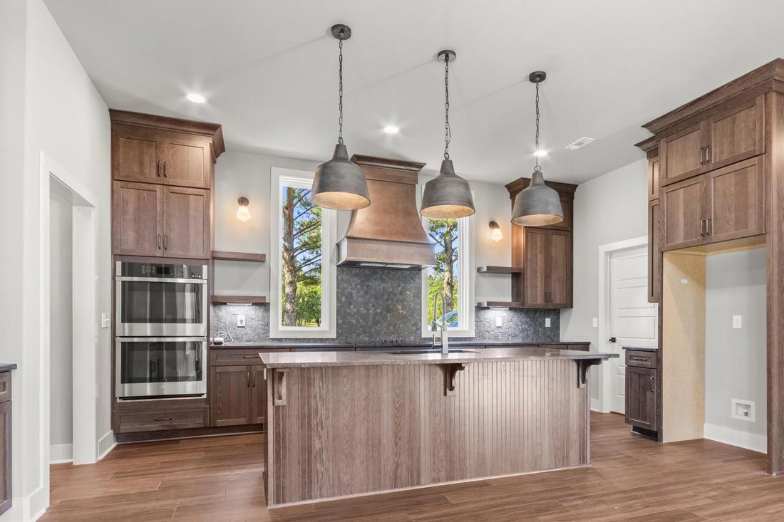 A kitchen featuring a large central island, brown wooden cabinets, stainless steel double ovens, and three pendant lights.