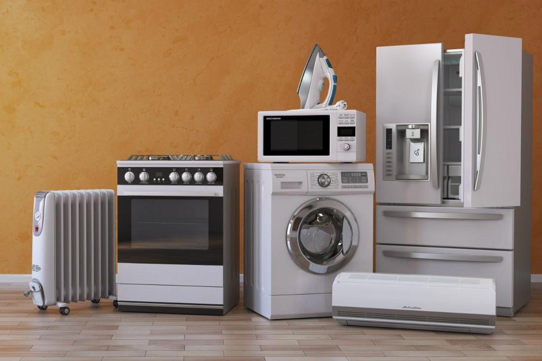 A variety of white and silver household appliances, including a fridge, stove, and washing machine, against an orange wall.