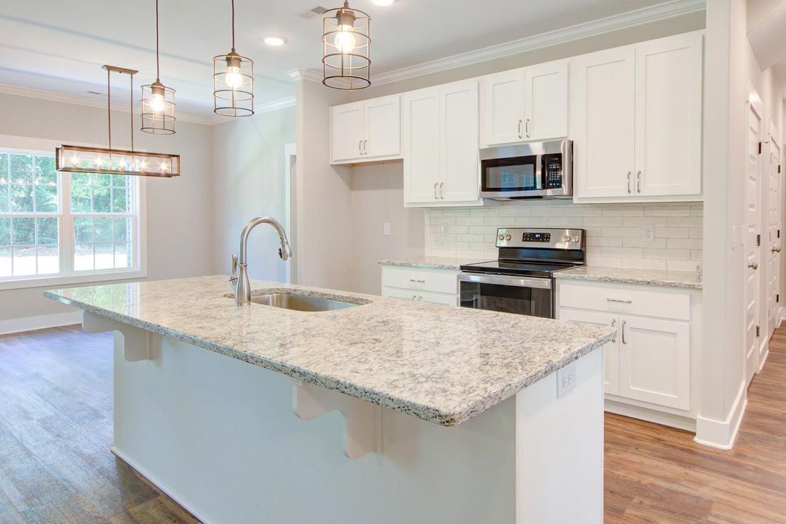 A modern, bright kitchen featuring a large granite island, white cabinets, stainless steel appliances, and wood flooring.