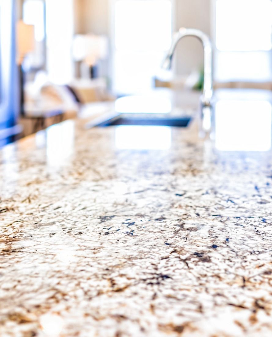 Close-up of a speckled granite kitchen countertop with a blurred sink and faucet in the background.