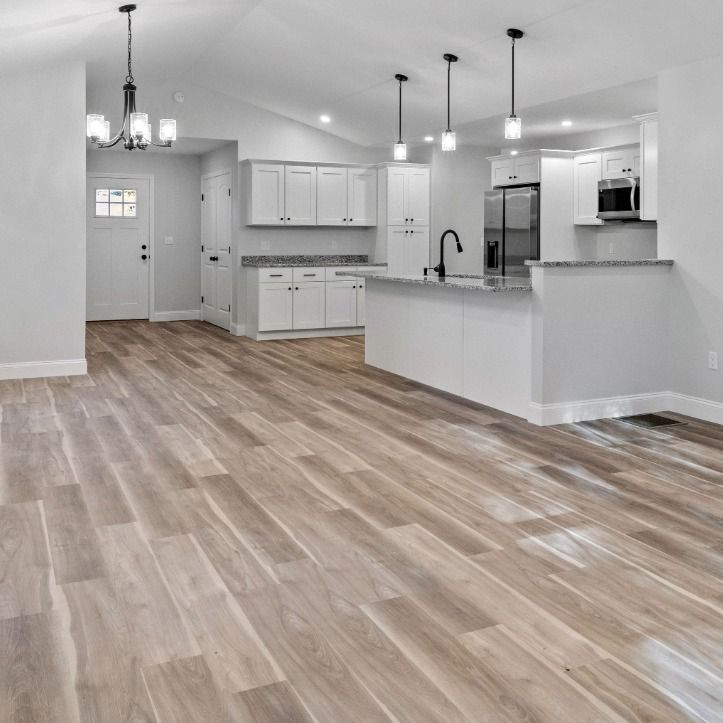 A modern, open-concept kitchen with white cabinets, a central island, stainless appliances, and light wood plank flooring.