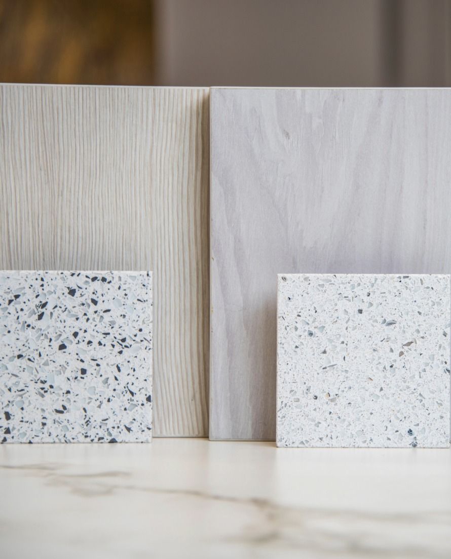 Two wood-grain samples and two speckled stone tiles displayed on a marble surface.