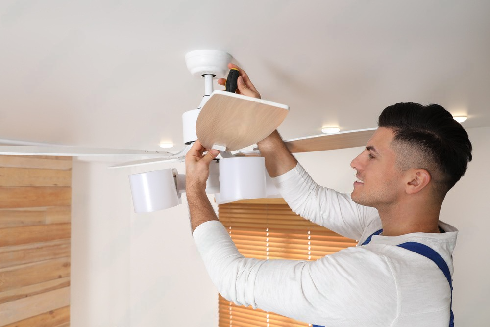 a man is installing a ceiling fan in a living room .