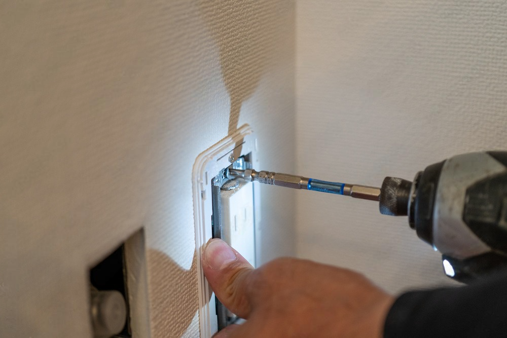 a person is using a drill to install a light switch on a wall .
