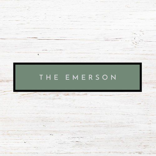 A green sign with the name the emerson on it is on a white wooden surface.