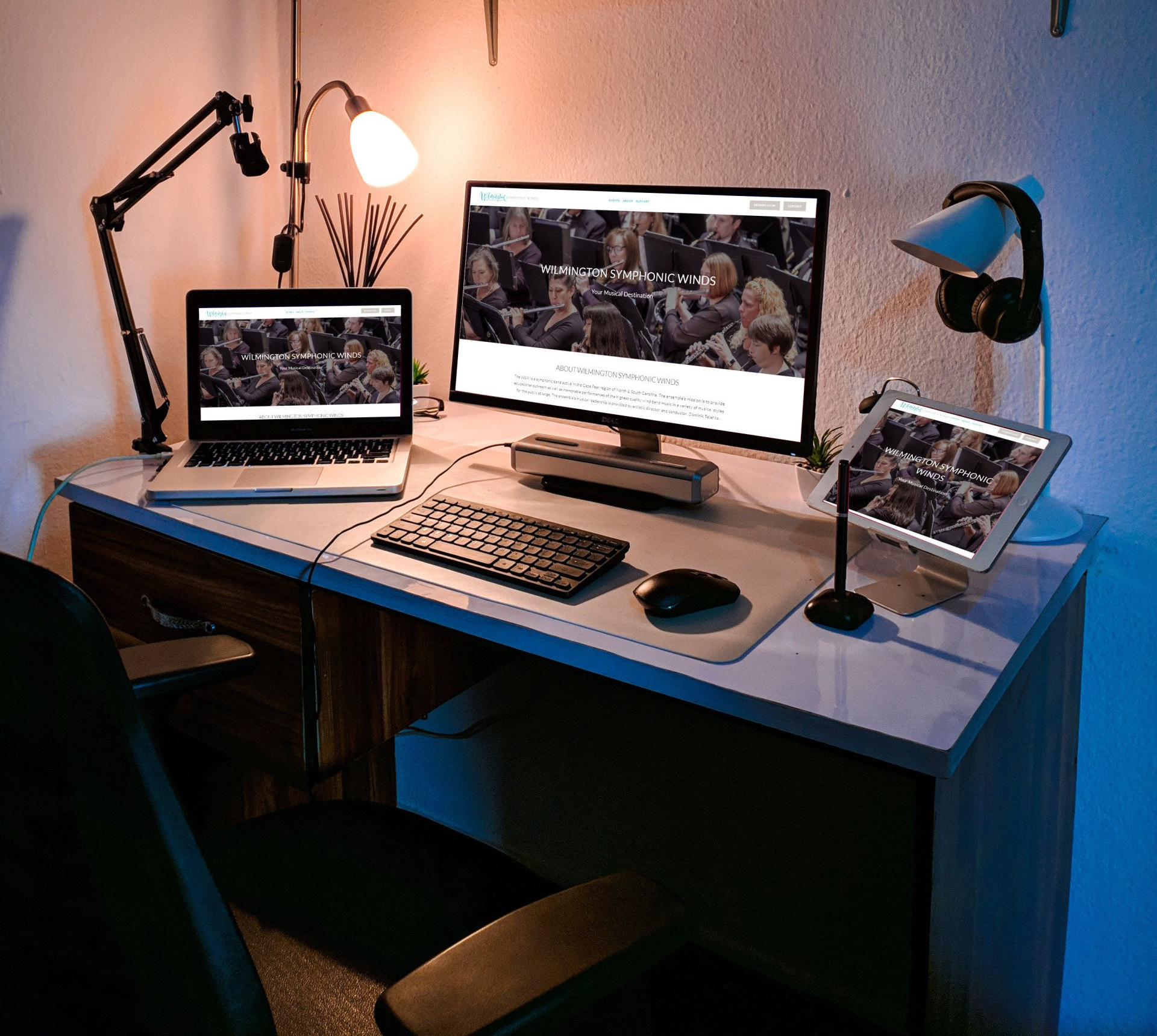 A desk with a computer monitor a laptop and a tablet