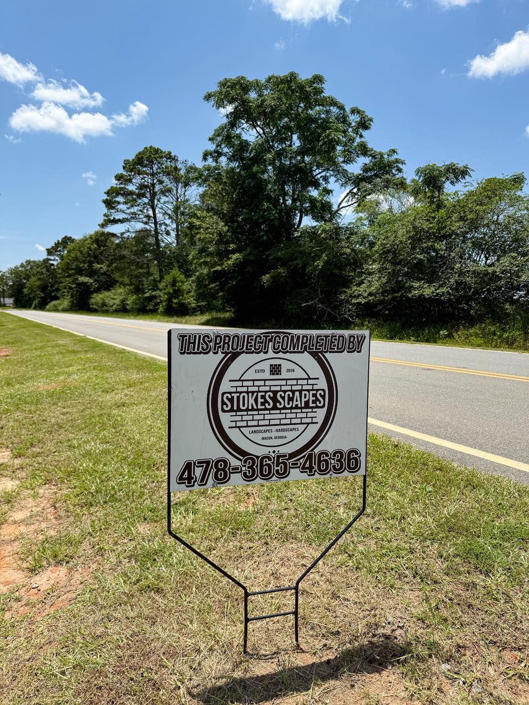 Sign for Stokes Scapes with phone number on a roadside in front of trees.