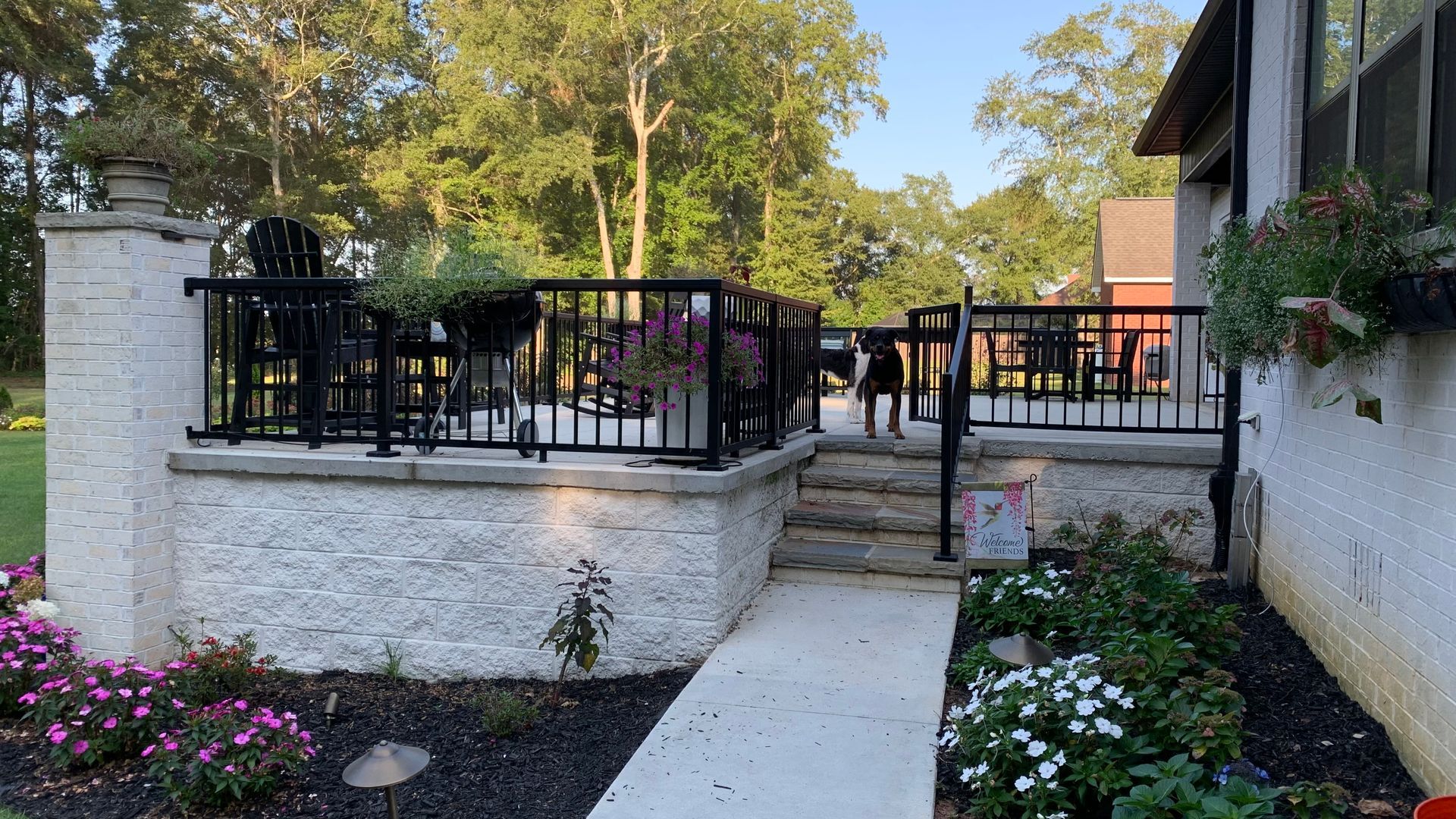 Backyard patio with black railings, steps, white textured walls, and flowerbeds.