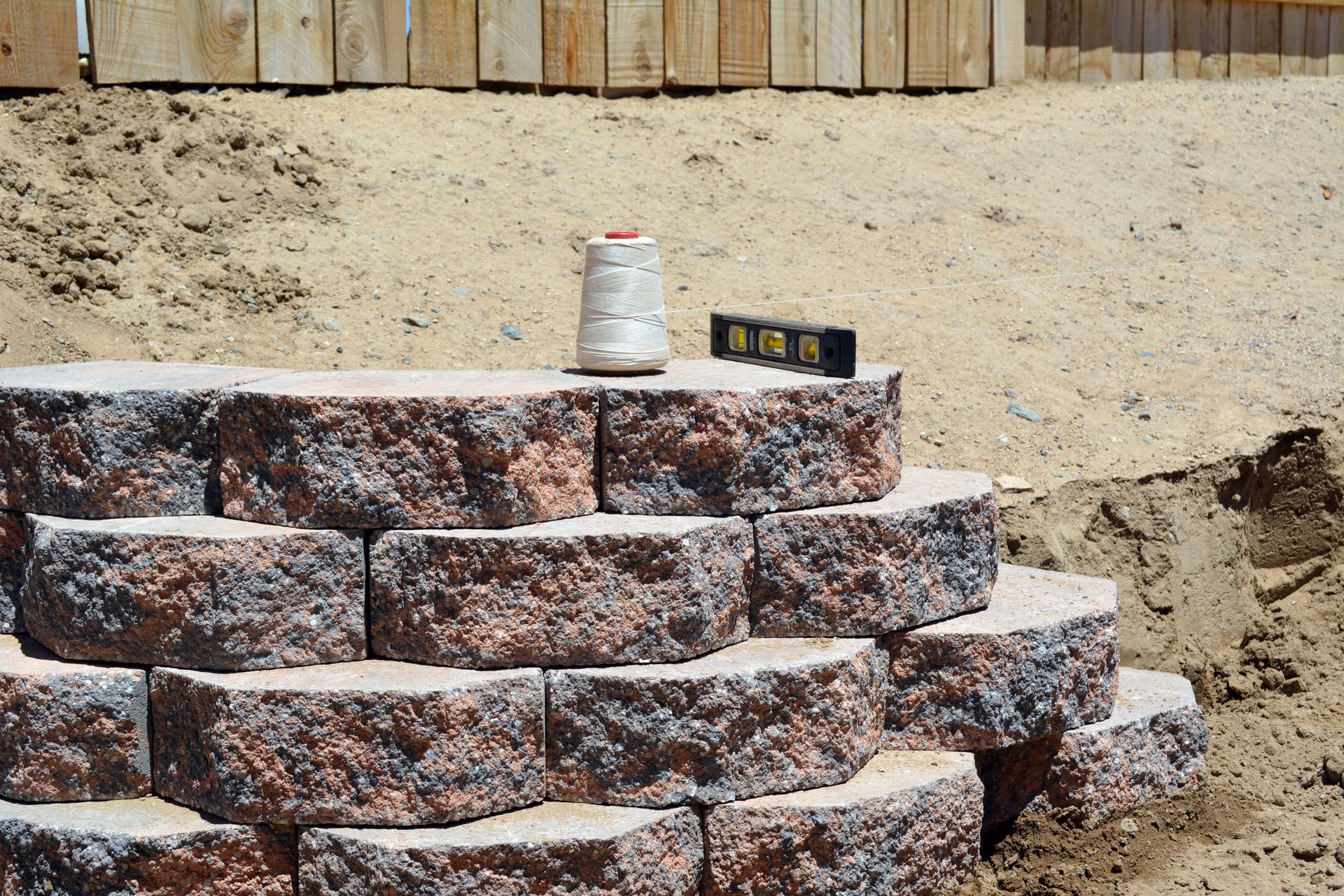 Stone retaining wall under construction with stacked blocks, sand, and a bucket on top Stone retaining wall under construction with stacked blocks, sand, and a bucket on top