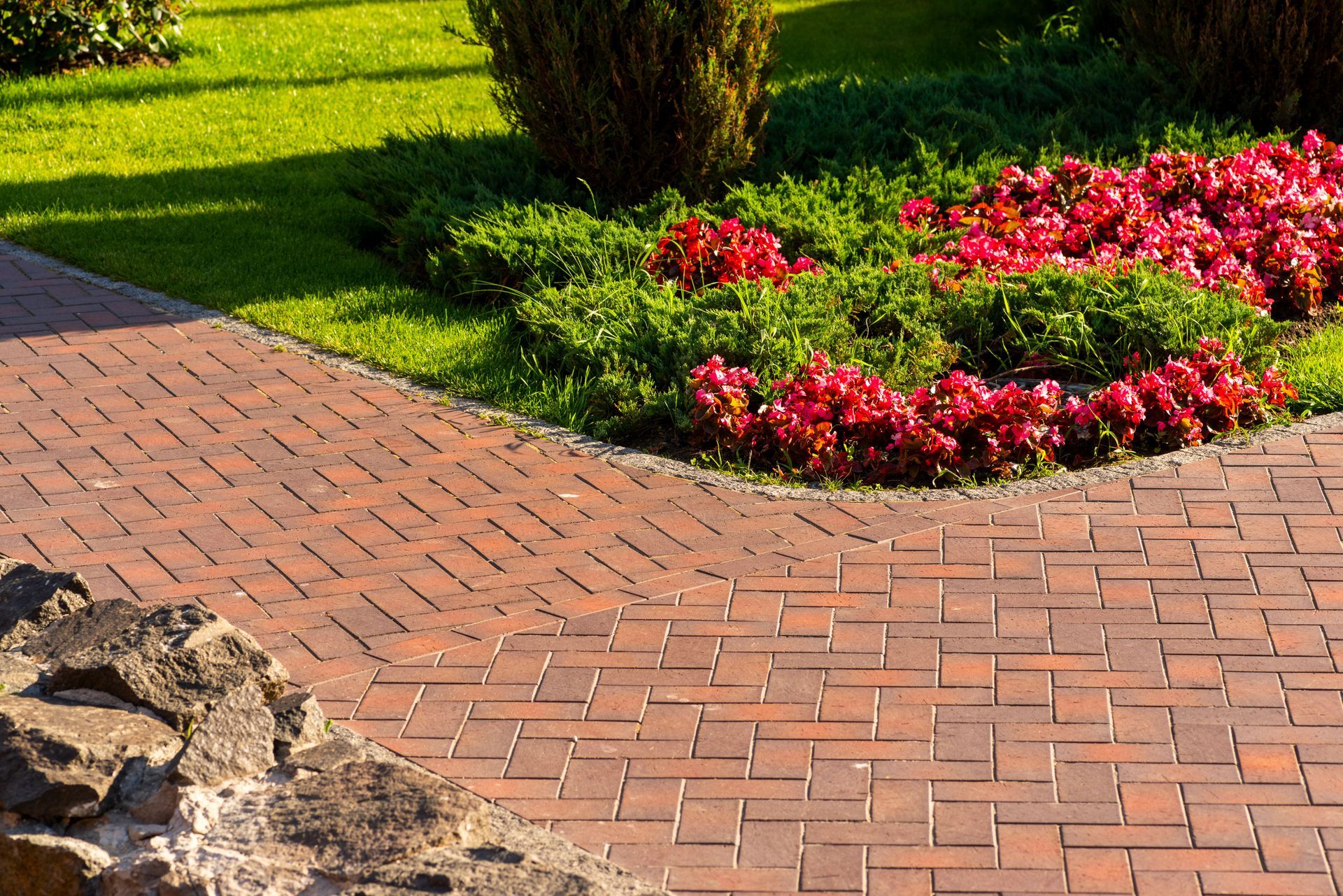 Brick garden path beside green lawn and red flower beds Brick garden path beside green lawn and red flower beds