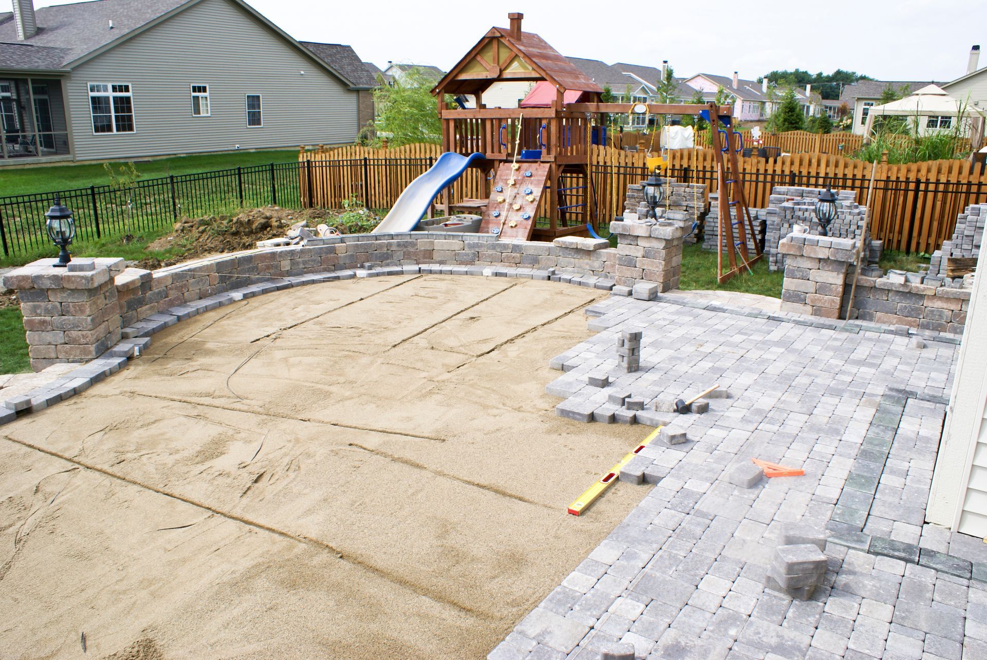 Backyard with an unfinished concrete patio, stone pavers, and a wooden playset with slide and swings Backyard with an unfinished concrete patio, stone pavers, and a wooden playset with slide and swings