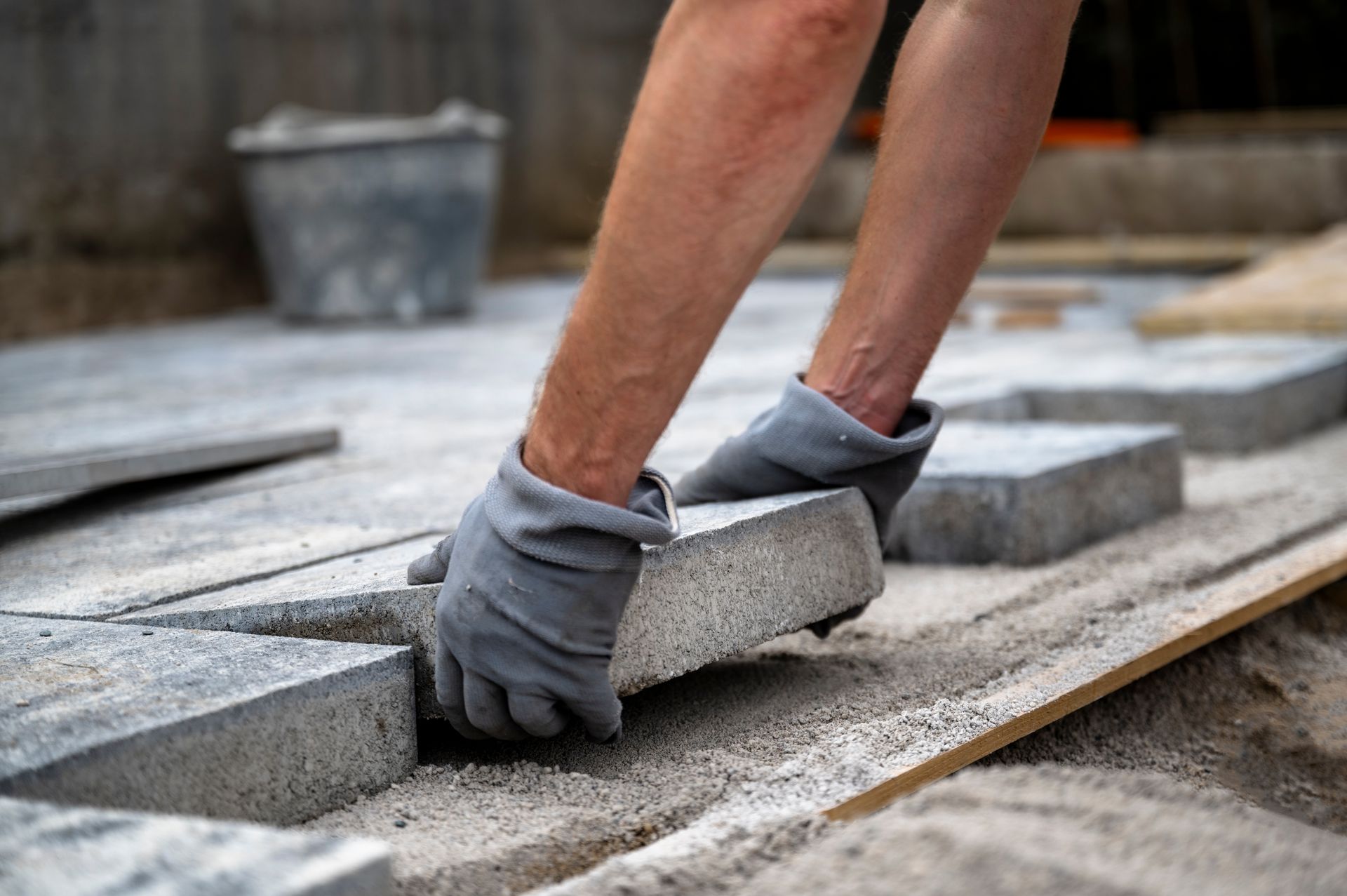Worker laying concrete pavers on a patio with gray gloves and a trowel Worker laying concrete pavers on a patio with gray gloves and a trowel