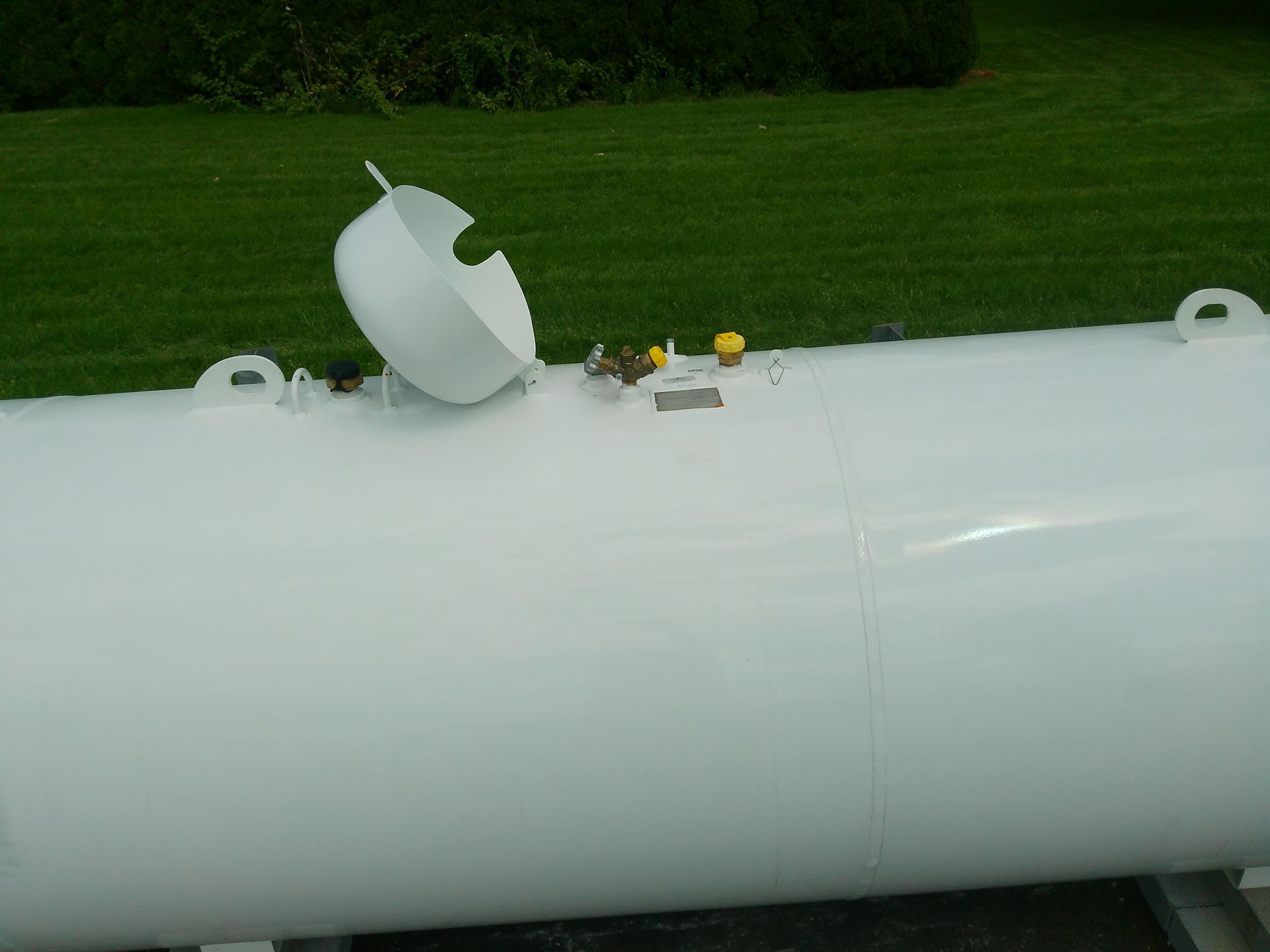 A Large White Tank with A Broken Lid Sits in The Grass