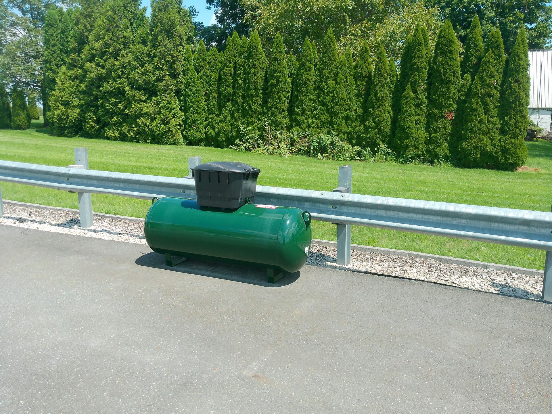 A Green Tank Sits on The Side of A Road with Black on Top