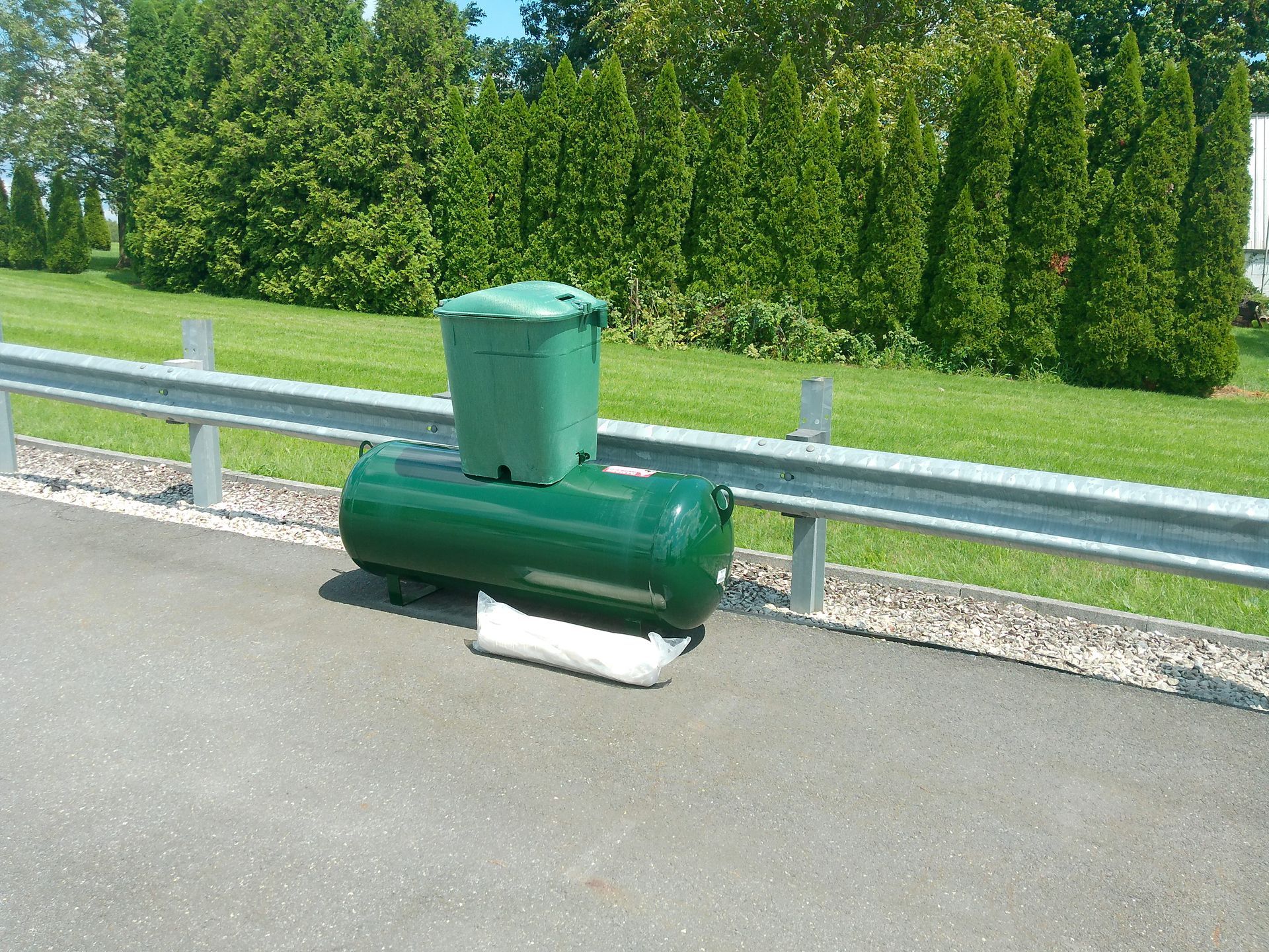 A Green Trash Can Sits Next to A Green Tank on The Side of A Road