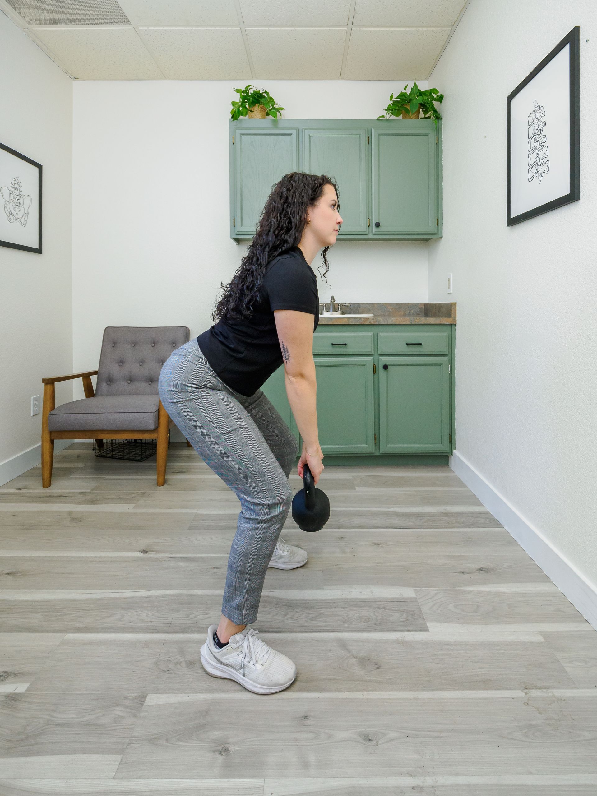 A woman is squatting with a kettlebell in a room.