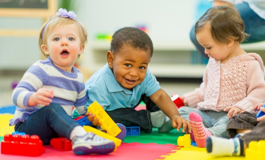 Three babies are sitting on the floor playing with toys.