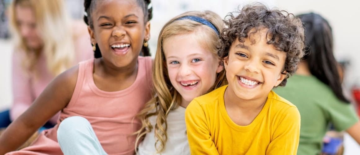 A group of children are sitting on the floor together and smiling for the camera.