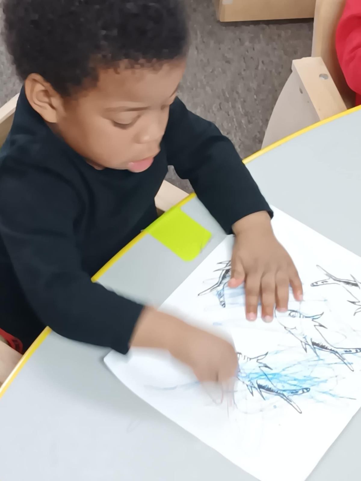 A young boy is sitting at a table playing with a piece of paper