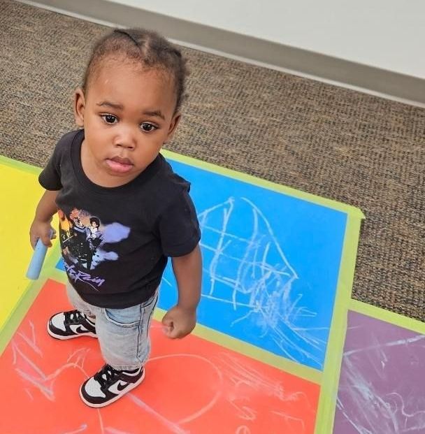 A little girl is standing on a colorful mat with chalk on it.