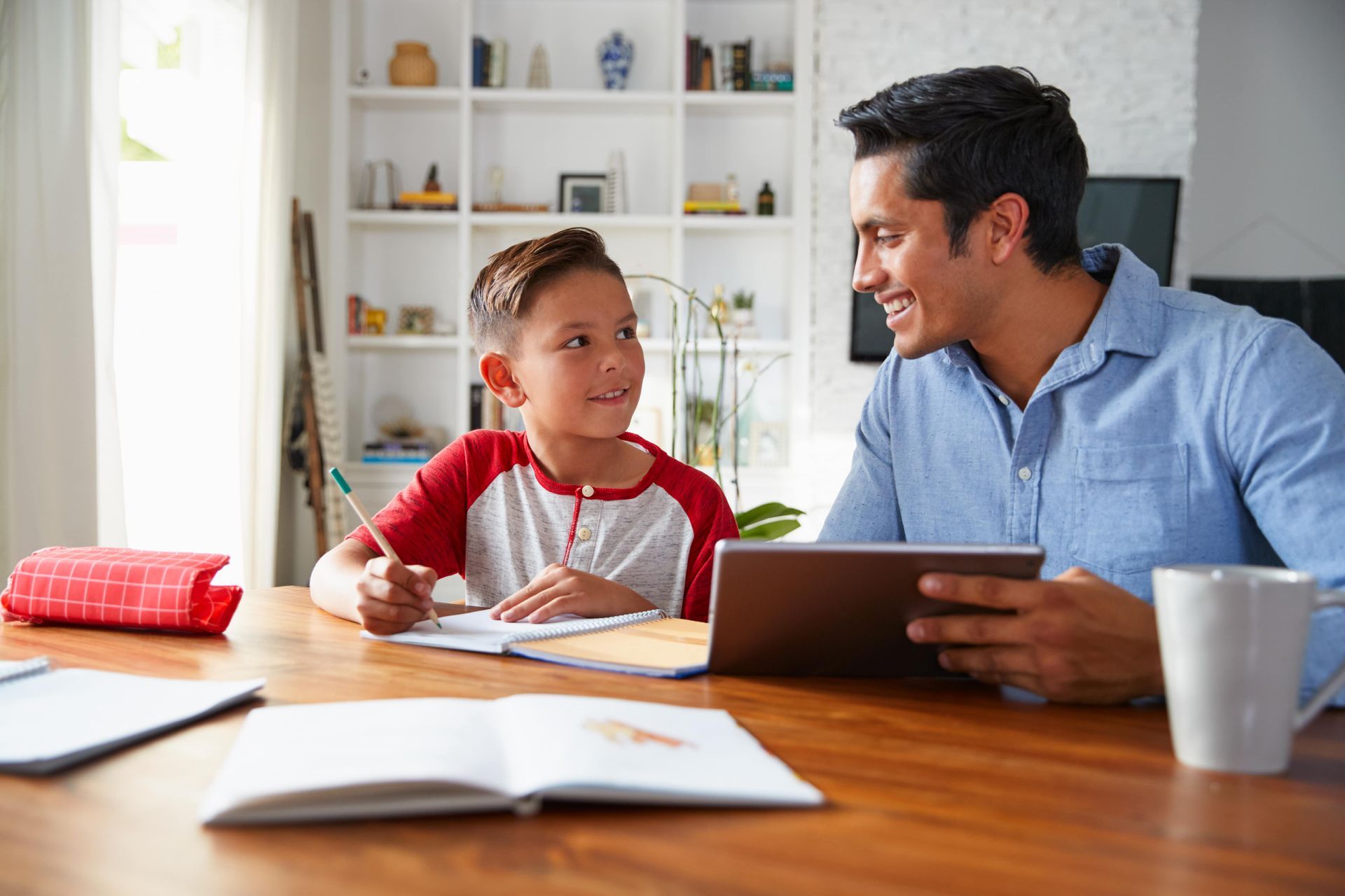 A father is helping his son with his homework while using a tablet computer.