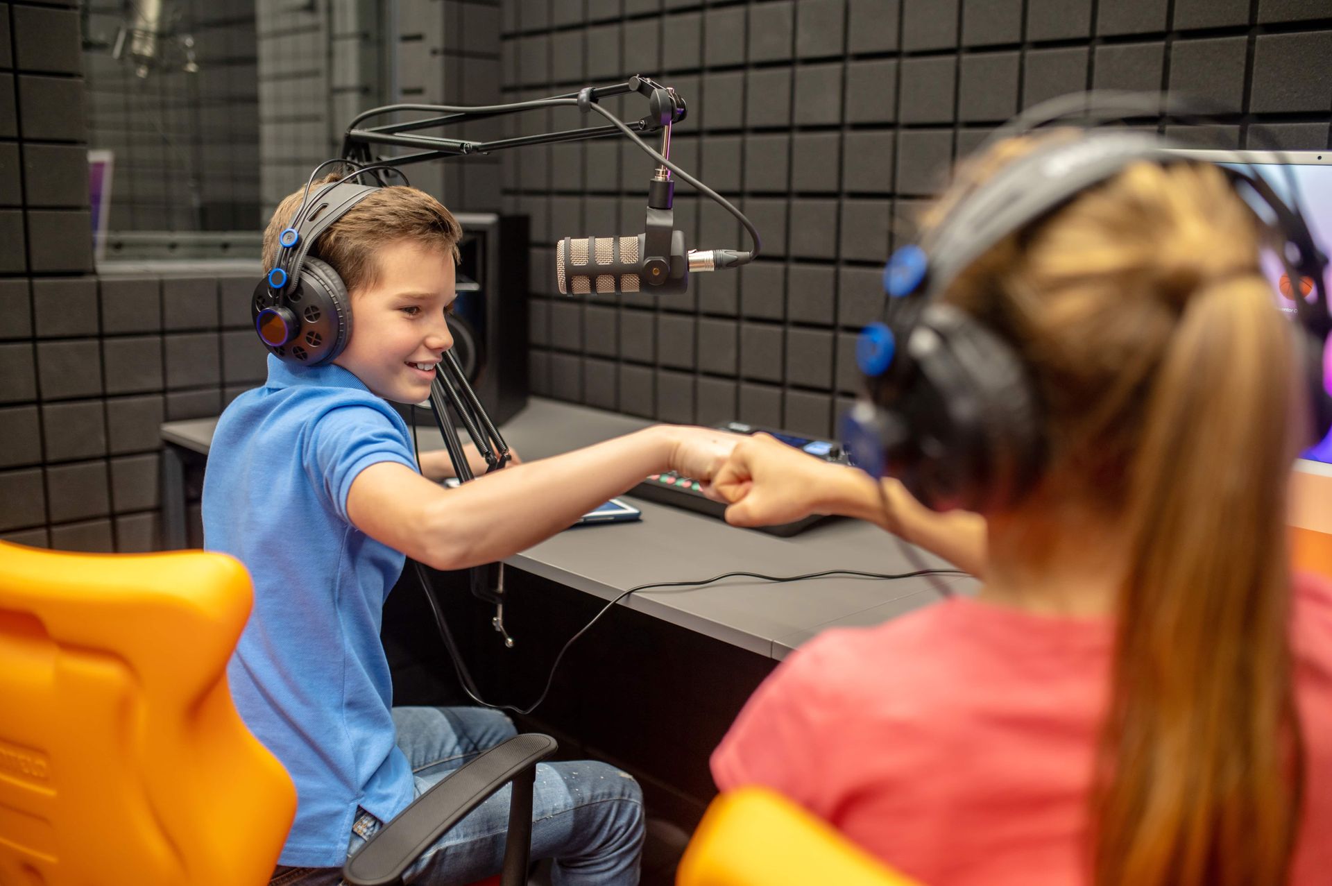 A boy and a girl are sitting in front of a microphone in a recording studio.