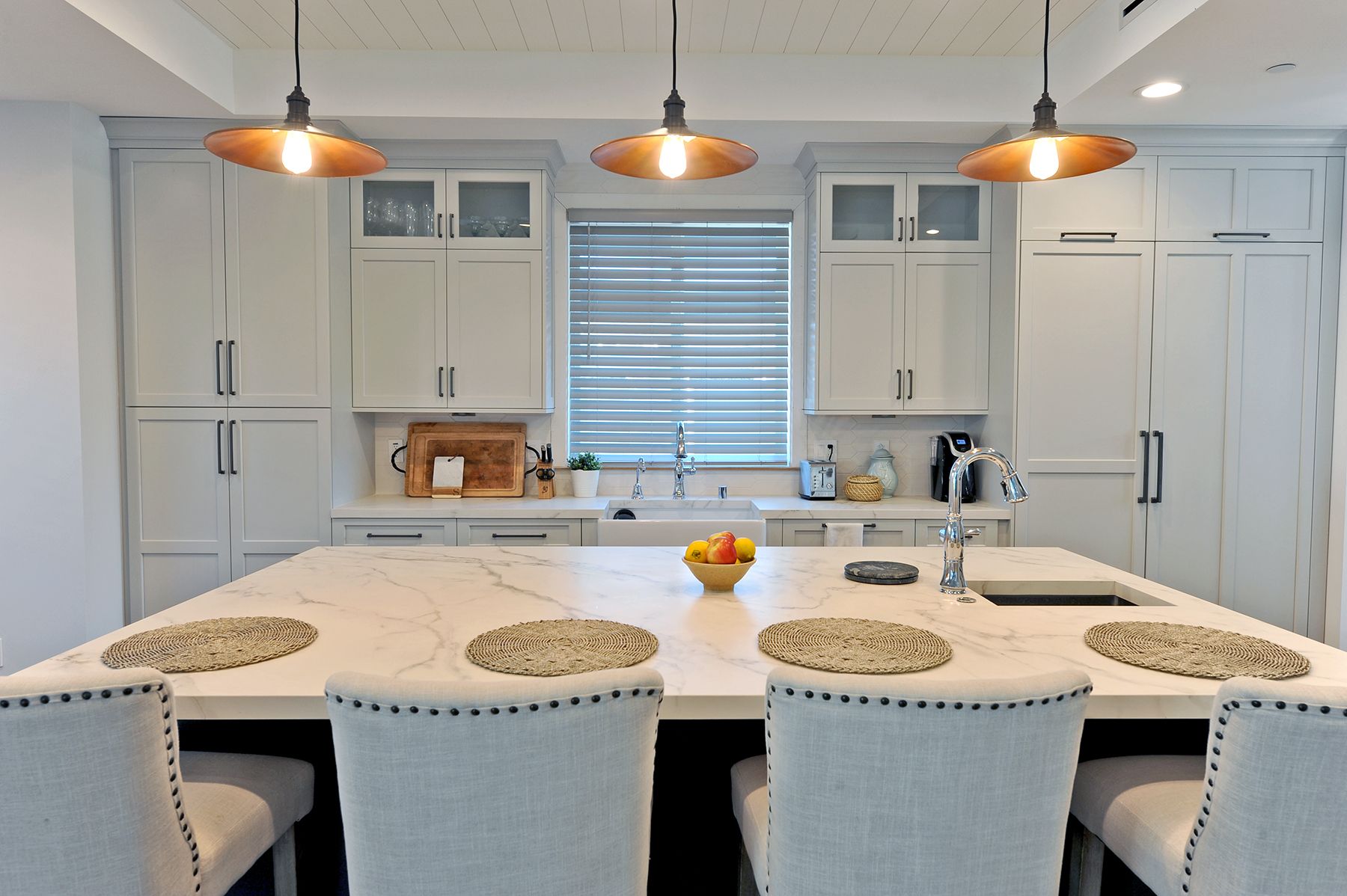 Kitchen with a large island, cabinets, three pendant lights, and several chairs.