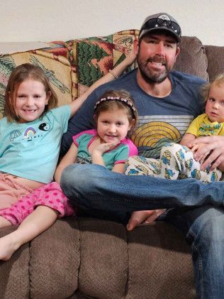 Man sits with three children on a couch. They smile and look at the camera.