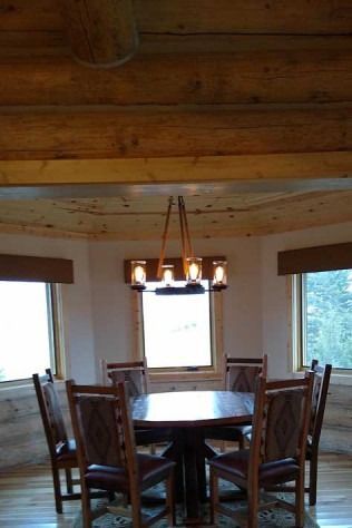 Dining room with a wooden round table, six chairs, and a chandelier; natural light.