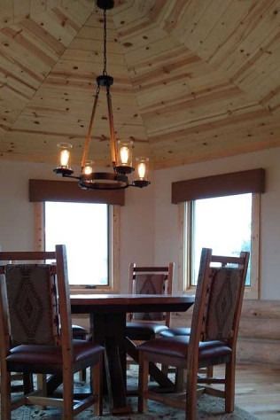 Dining room with wooden table, chairs, and chandelier; windows and wood ceiling.