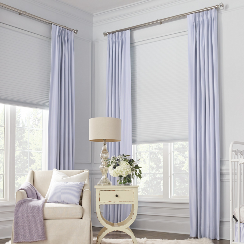 Bedroom with sheer curtains and white shades, soft colors, chair, side table with lamp, and a crib.