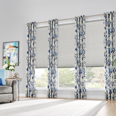 Room with blue patterned curtains, gray blinds, artwork, and a gray couch.