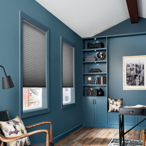 A home office with blue walls, windows with gray blinds, built-in shelves, and a wooden floor.