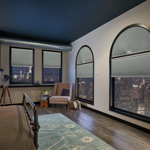 Bedroom with arched windows and city view, blue rug, neutral walls, dark ceiling, and industrial style bedframe.