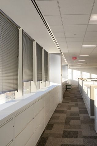 Office hallway with cubicles, windows with blinds, and carpeted floor.