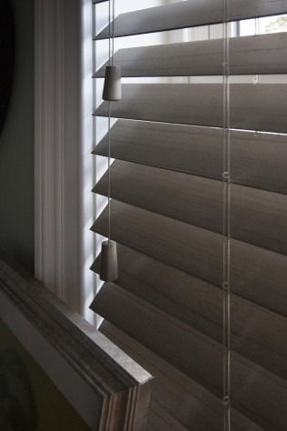 Wooden blinds partially open, casting shadows. Close-up view of the slats, string, and control knobs.