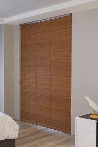 Brown wooden panel blinds covering a doorway in a room with a bed and a nightstand.