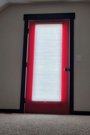 Red door with white window blinds, black frame, in a room with beige walls and carpet.