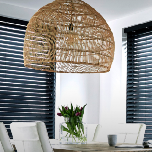 Large woven pendant light above a dining table set with white chairs and purple flowers.