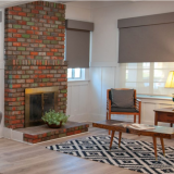 Living room with brick fireplace, gray shades, wooden furniture, and patterned rug.