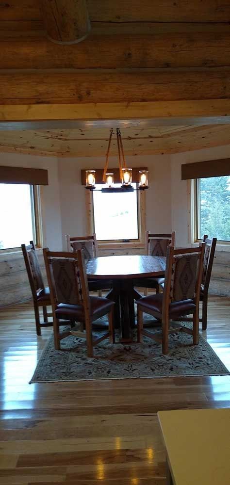 A rustic dining room with a round table, six chairs, and a chandelier, situated on a rug.