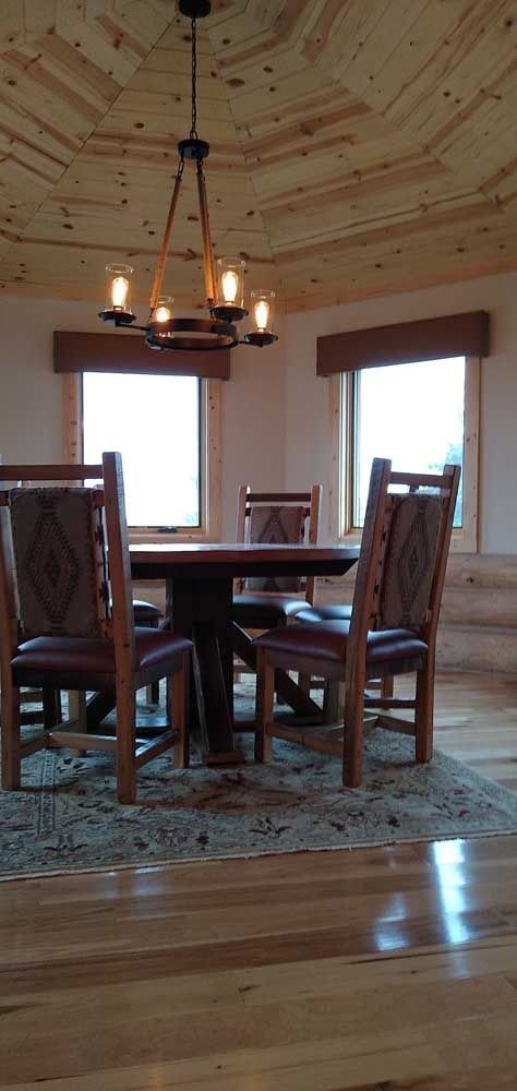 Dining area with round table, four chairs, chandelier, and windows, wood ceiling and flooring.