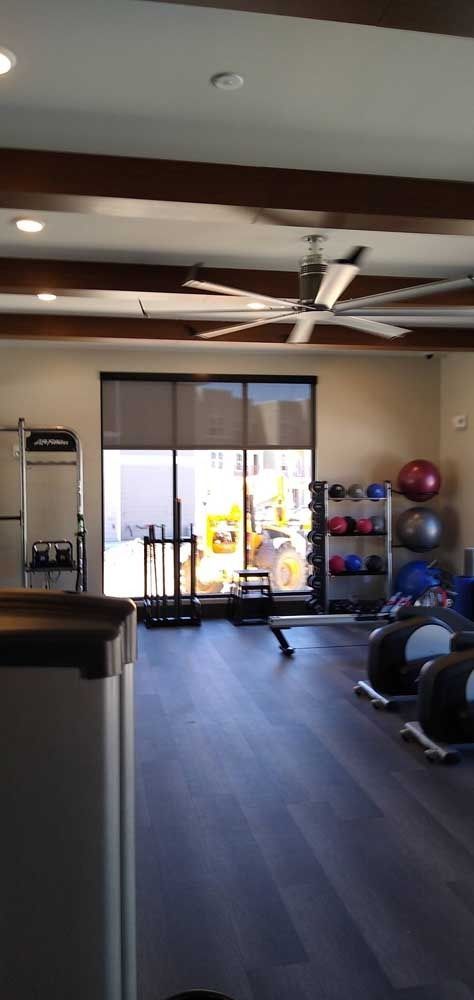 A gym interior with exercise equipment, large windows, and a ceiling fan.