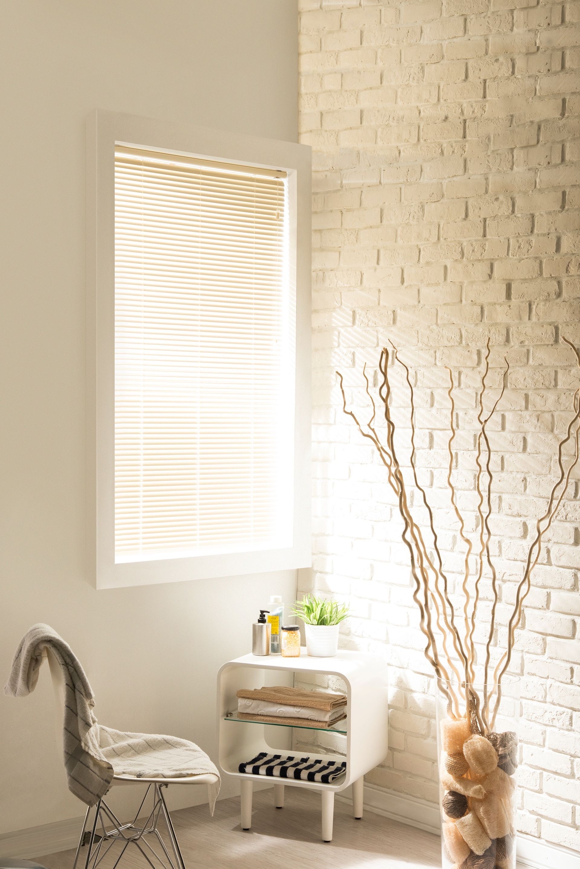 A bright, minimalist room with a window, white brick wall, chair, and decorative vase.