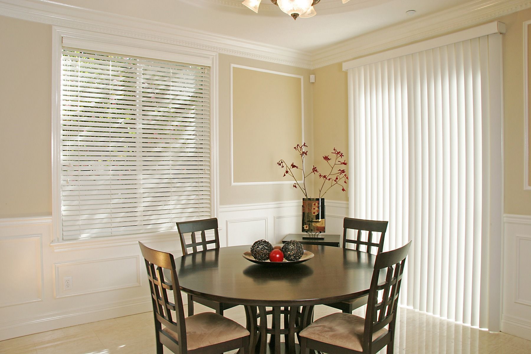 Dining room with a round dark table and four chairs, tall vertical blinds, window with horizontal blinds.