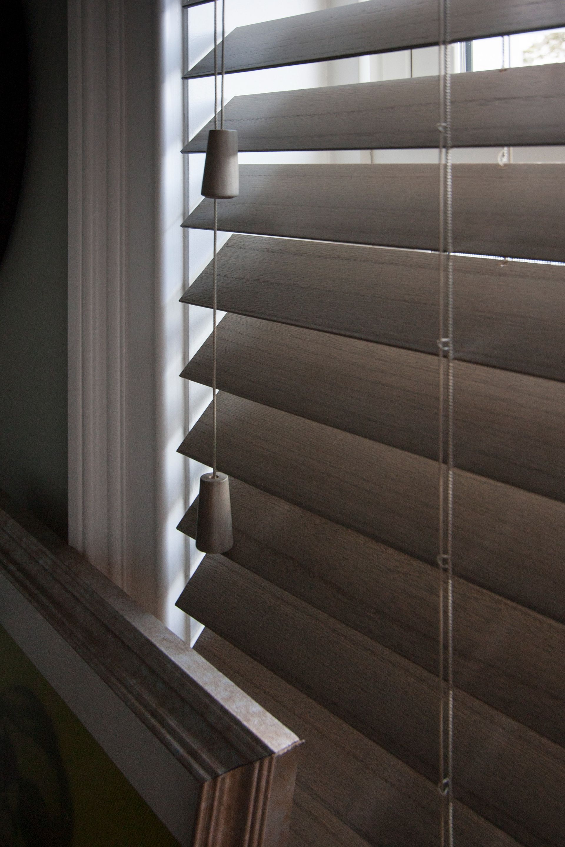 Wooden blinds in a window, partially closed, allowing some light to pass through.