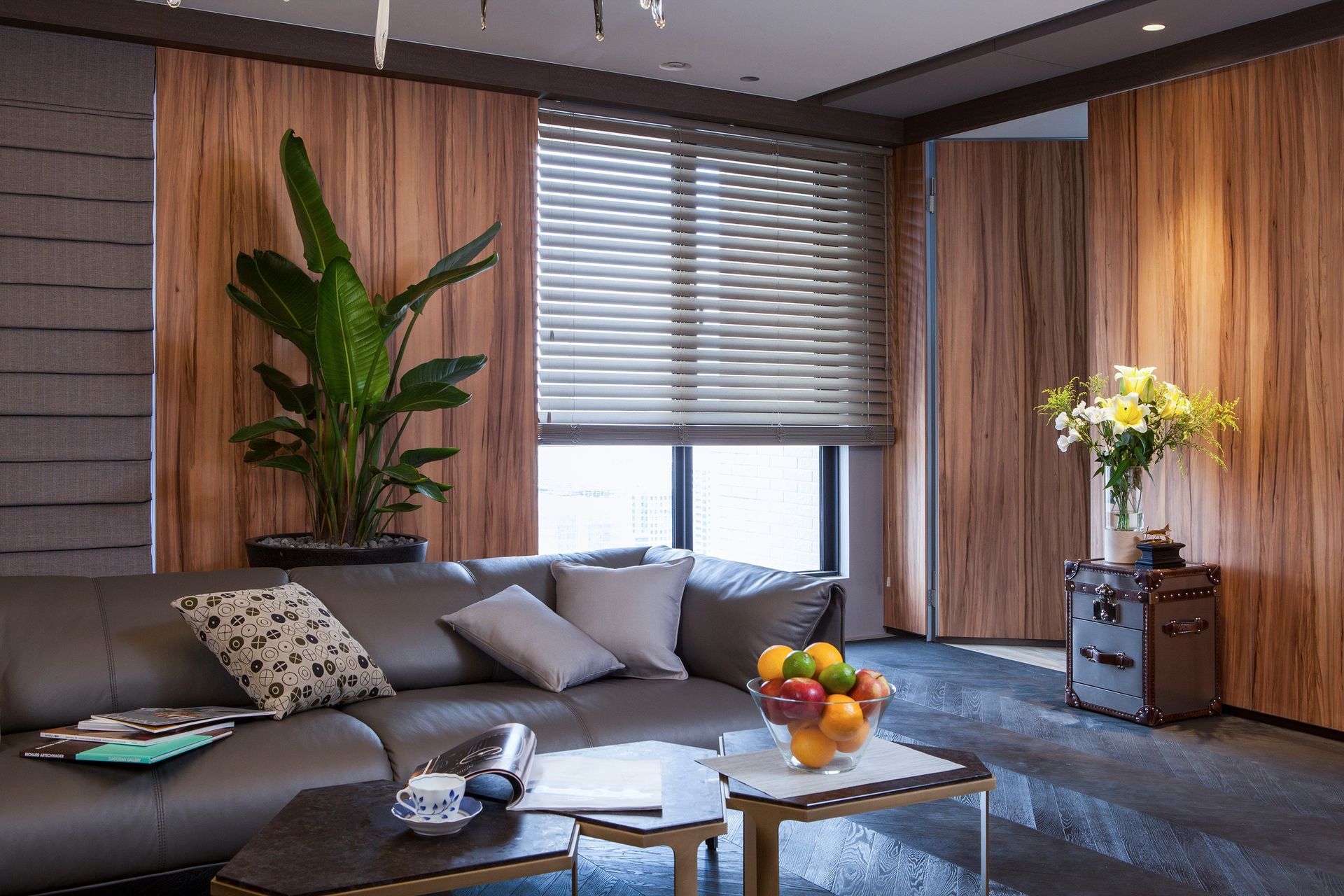 Living room with leather sofa, wooden paneling, blinds, large plant, and fruit.