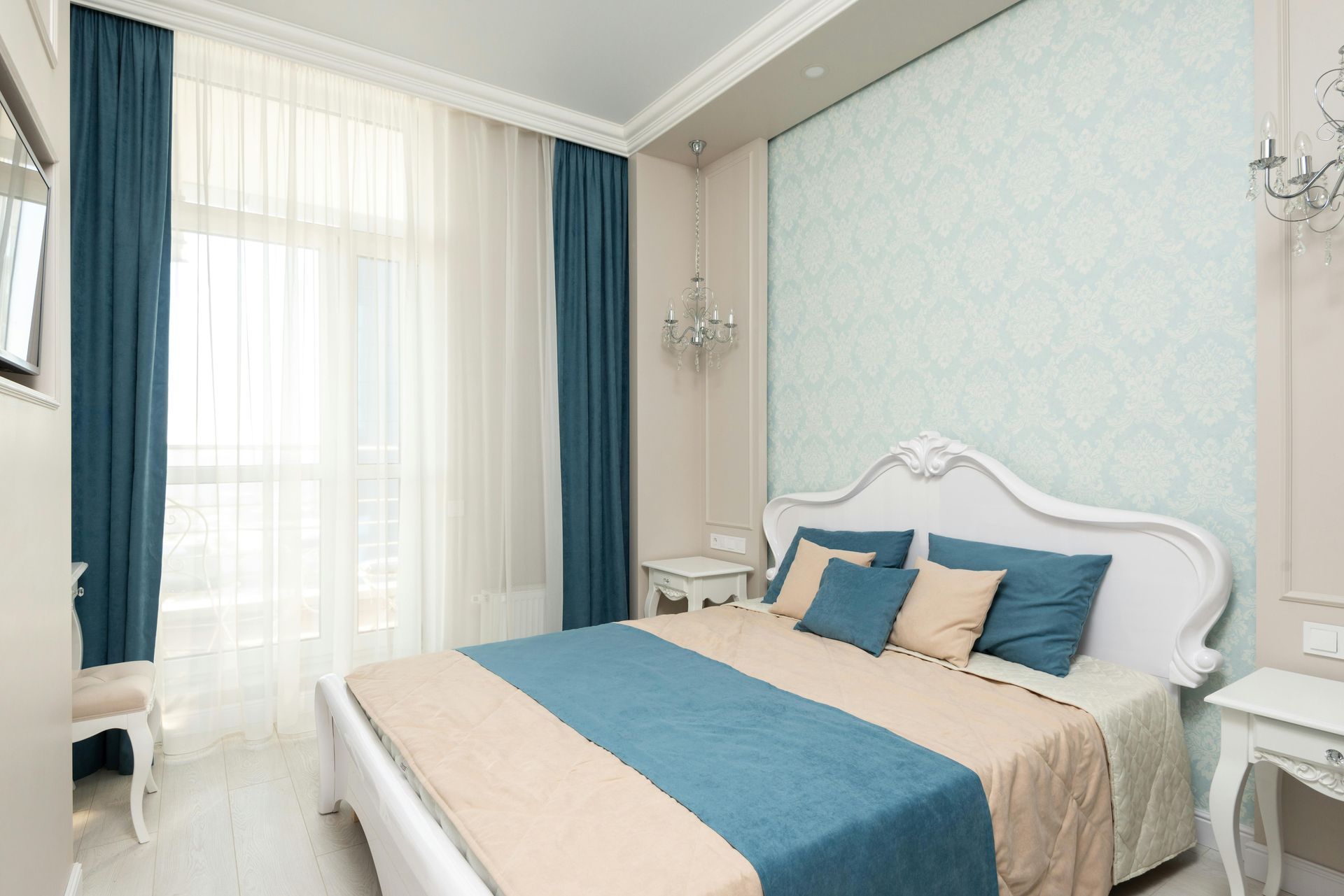 Bedroom with blue and beige accents; bed with ornate headboard, sheer curtains, and side tables.